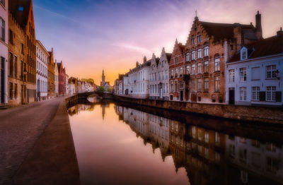 Canal amidst buildings against sky during sunset in city