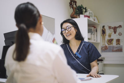 Happy female doctor wearing eyeglasses discussing with patient in medical clinic