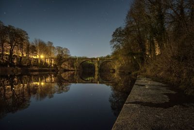 Reflection of trees in water against clear sky at night