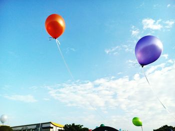 Low angle view of helium balloons flying against sky