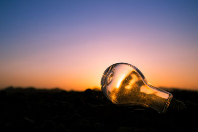 Close-up of light bulb on land against sunset sky