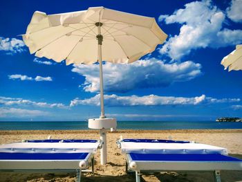 Deck chairs and parasols on beach against blue sky