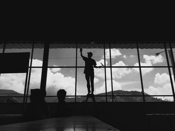 Silhouette people standing by window against sky