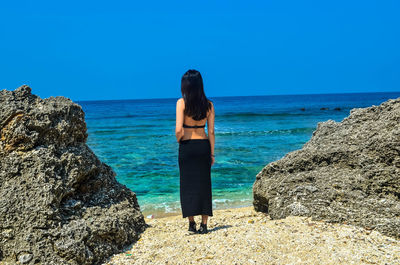 Woman standing on rock by sea against blue sky