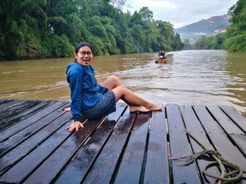 Portrait of smiling young woman sitting on jetty against lake