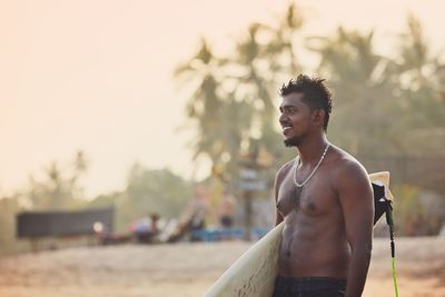 Young man holding surfboard looking away at beach