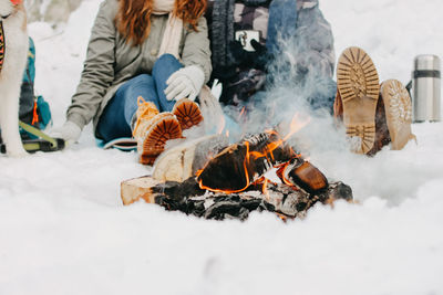 Low section of couple siting by bonfire on snow covered land