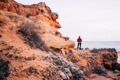 Rear view of woman standing on rock by sea against sky