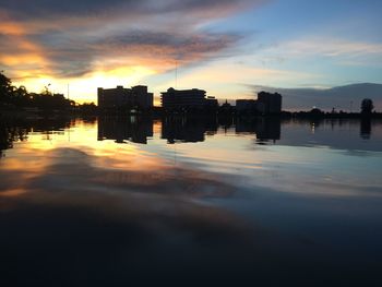Silhouette buildings by river against sky during sunset