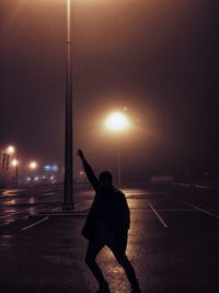 Silhouette man standing arms outstretched on wet street at night