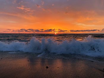 Waves rushing at beach against cloudy sky during sunset