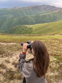 Rear view of a woman standing with binoculars in the mountains against the sky