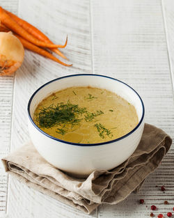 Healthy bone broth in a bowl with dill on a light wooden background.