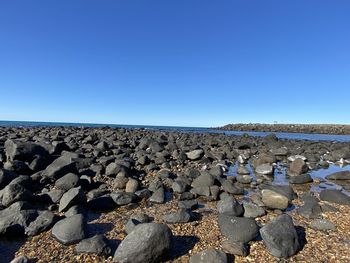 Rocks on shore against clear blue sky