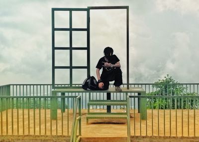 Man sitting on railing against sky