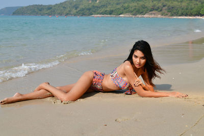 Portrait of young woman wearing bikini lying on beach