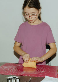 One girl bakes cookies, kneading the dough with her hands on the table.