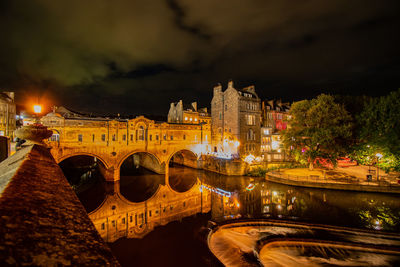 Illuminated bridge over river in city against sky at night