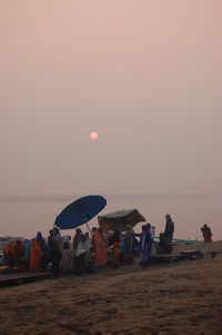 People at beach against clear sky during sunset