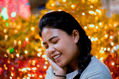 Smiling young woman against illuminated christmas tree at night