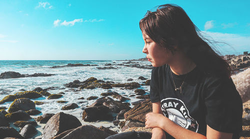 Side view of young woman looking at sea against sky