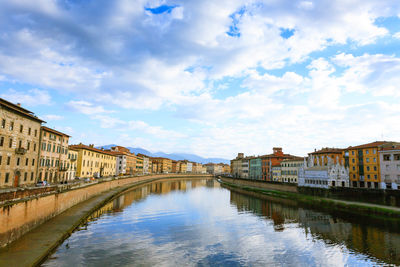 Arch bridge over canal amidst buildings against sky in city