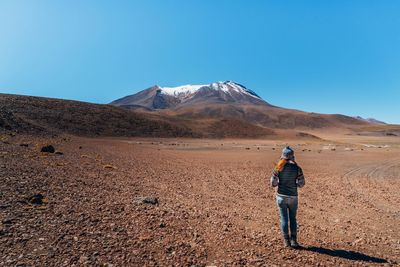 Rear view of man standing on desert against clear blue sky