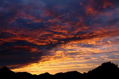 Scenic view of dramatic sky over silhouette mountains during sunset