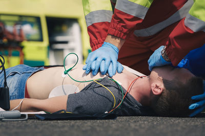 Hands of paramedic and doctor during resuscitation on road against ambulance car. 