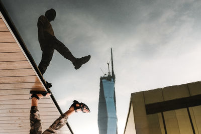 A reflection on still water of a man leaping over a skyscraper