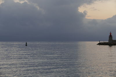 Lighthouse by sea against cloudy sky during sunset