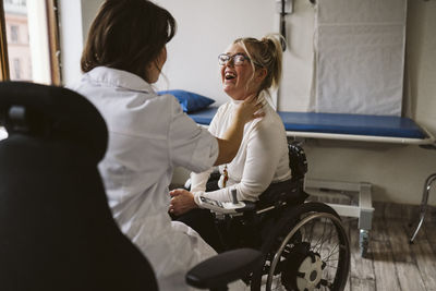 Female doctor checking pulse of smiling disabled patient at medical clinic
