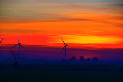 Silhouette wind turbines on land against sky during sunset