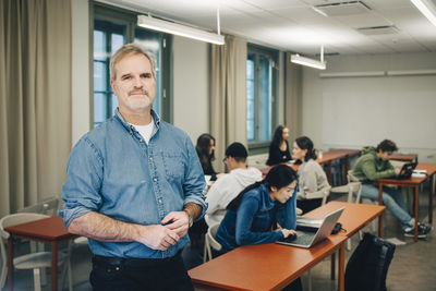 Portrait of male teacher with students studying at desk in classroom