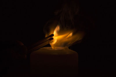 Cropped image of person igniting candle in darkroom