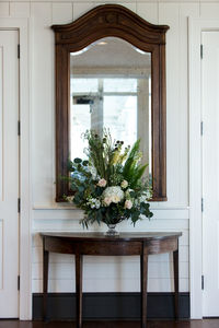 Flower vase on wooden table against mirror at home