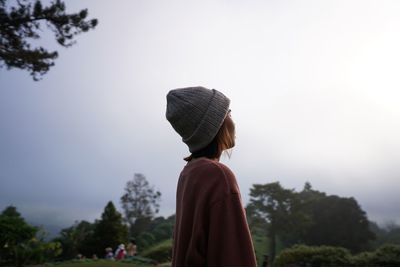 Side view of woman wearing warm clothing while standing in forest against sky