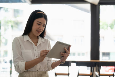 Young woman using mobile phone while standing in cafe