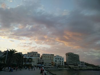 Cityscape by sea against sky during sunset