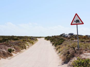 Animal crossing sign by dirt road against sky