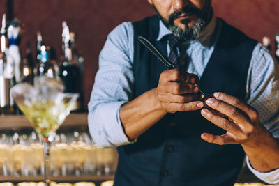 Midsection of mature bartender preparing cocktail in bar