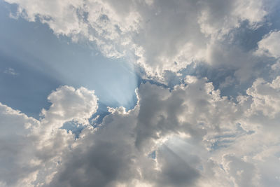 Low angle view of sunlight streaming through clouds