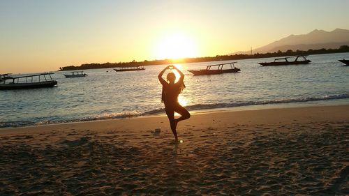 Silhouette woman making heart shape with hands while standing on one leg at beach