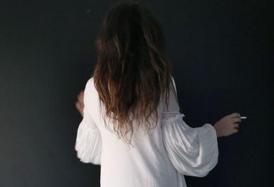 Rear view of woman holding cigarette while standing against black background