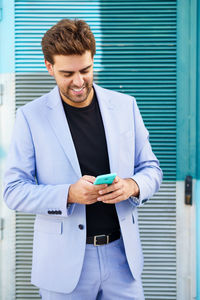 Smiling businessman using smart phone standing outdoors