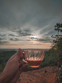 Midsection of man holding drink against sky during sunset