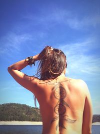 Rear view of naked woman with dreamcatcher tattoo on back against sky