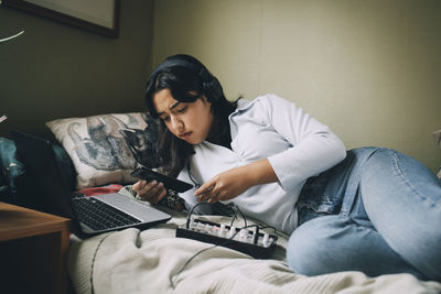 Teenage girl using mobile phone and laptop while lying on bed at home