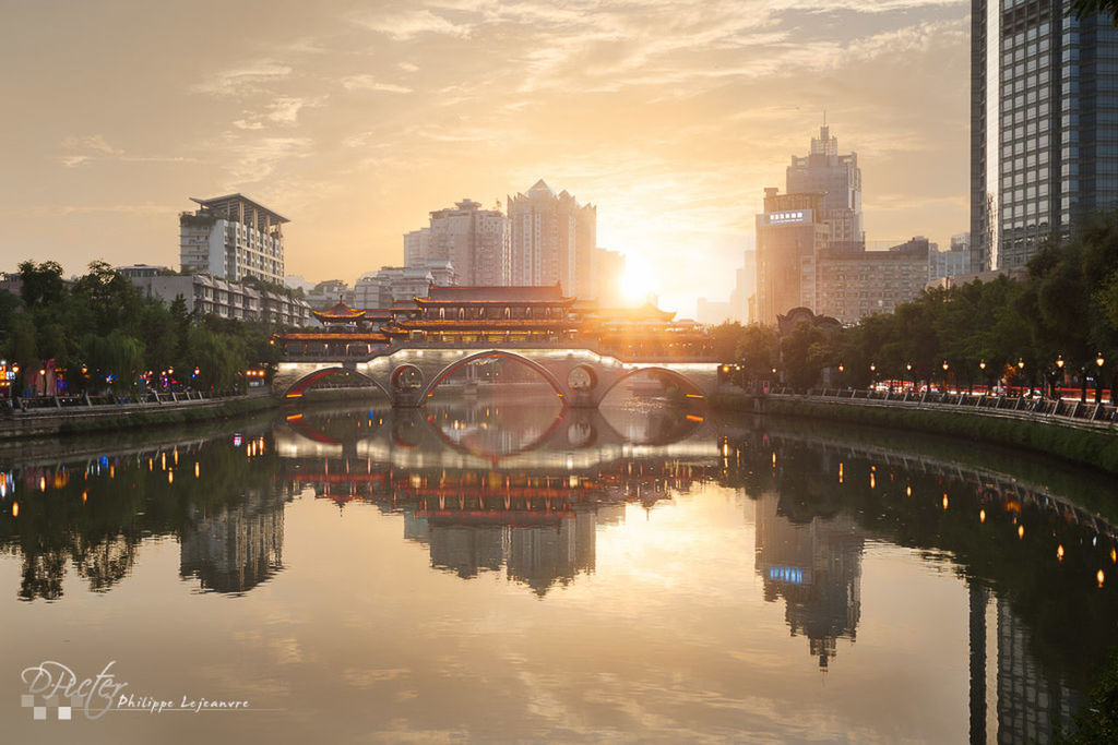 architecture, built structure, building exterior, reflection, city, water, sunset, river, connection, bridge - man made structure, sky, sun, waterfront, tree, cityscape, arch bridge, city life, sunlight, canal, cloud - sky