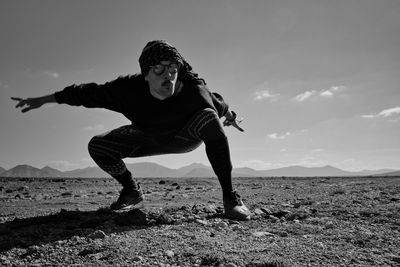 Full length of man crouching on ground against sky